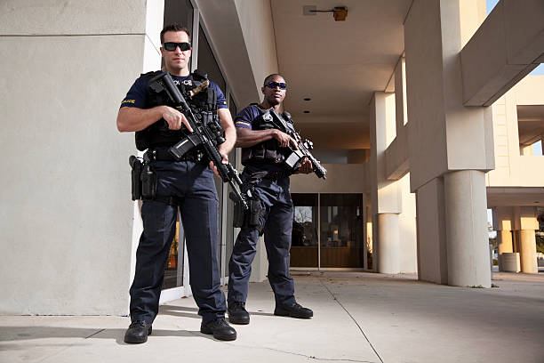 Multi-ethnic police officers (20s) wearing bulletproof vests, holding rifles.